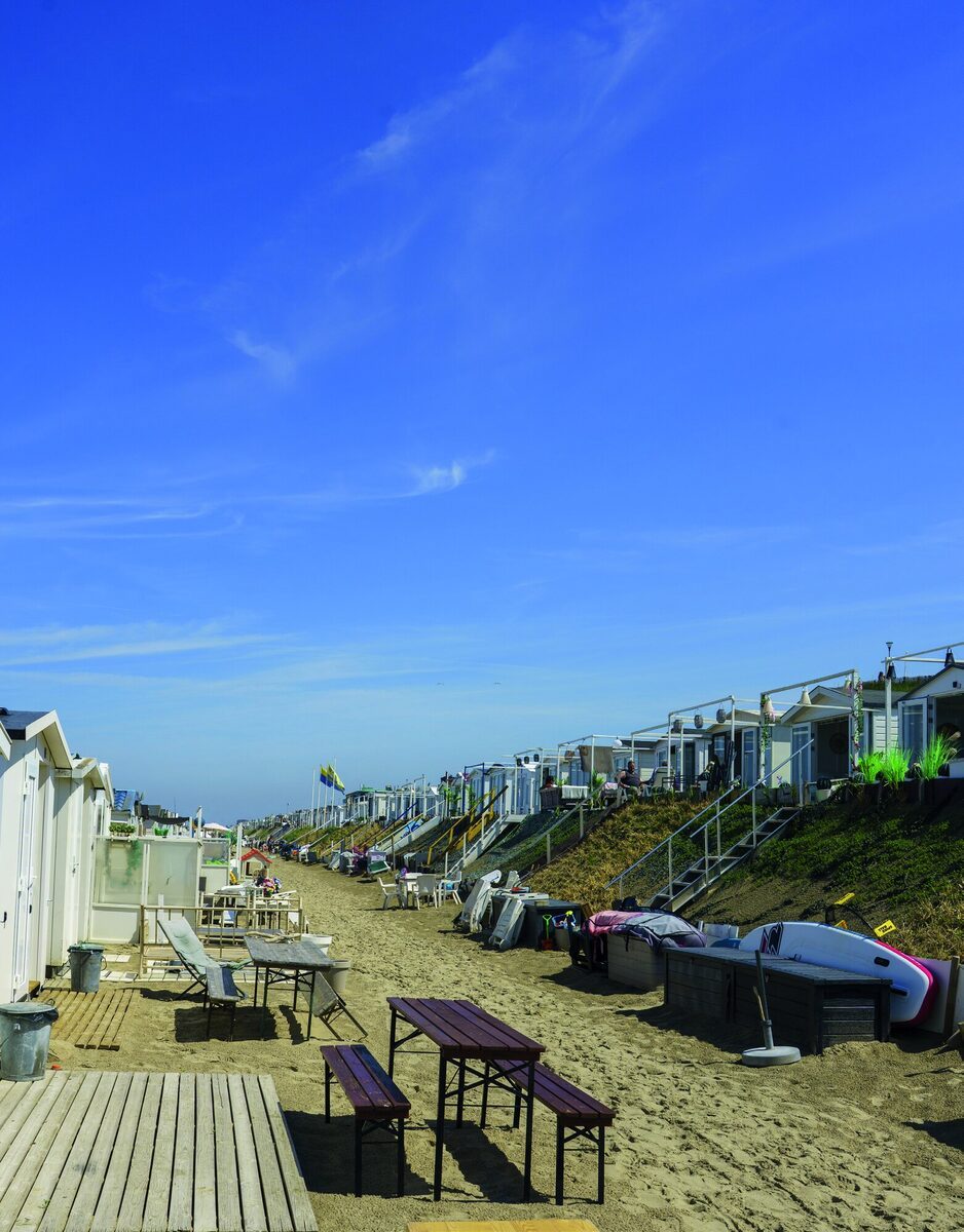 Strandhuisjes op een rij op het strand van Zandvoort, met bewoners op hun terras aan zee
