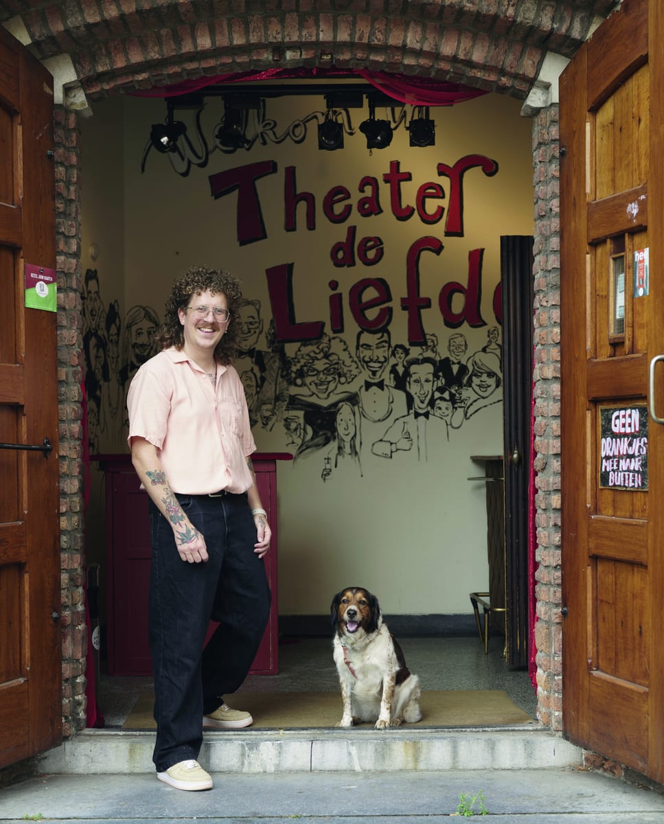 Mees van Haren met een hond in de open deur van Theater de Liefde, voor de beschilderde muur