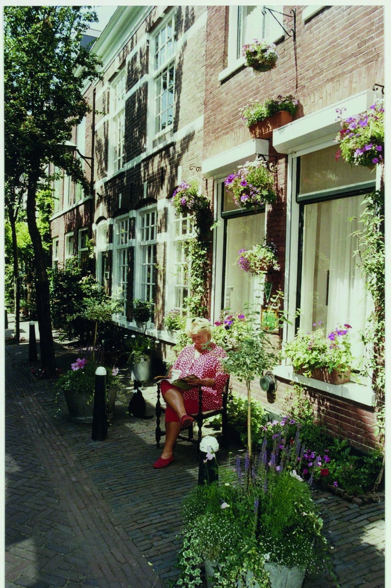 Een vrouw in een rode jurk leest op een stoel voor een huis in de bloemrijke Korte Houtstraat